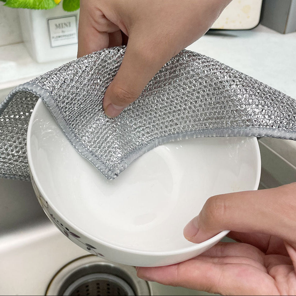 Person cleaning a white bowl with a metallic scrubber in a kitchen setting.