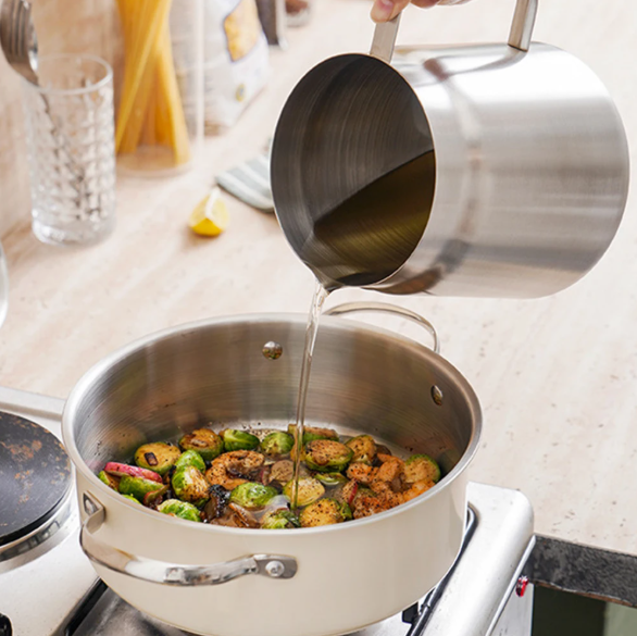 Stirring vegetables in a stainless steel oil pot strainer on a stove