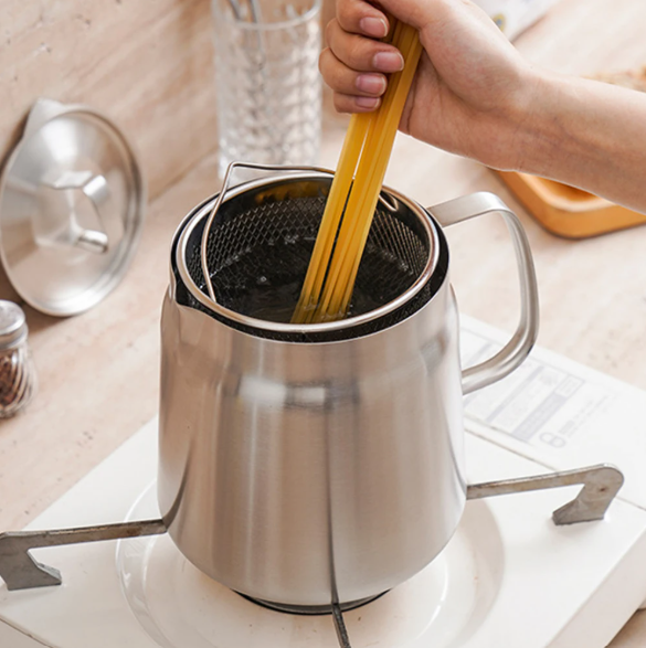 Stainless steel oil pot strainer with a hand holding a wooden spoon over it on a kitchen counter.
