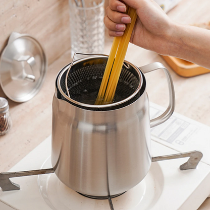 Stainless steel oil pot strainer with a hand holding a wooden spoon over it on a kitchen counter.